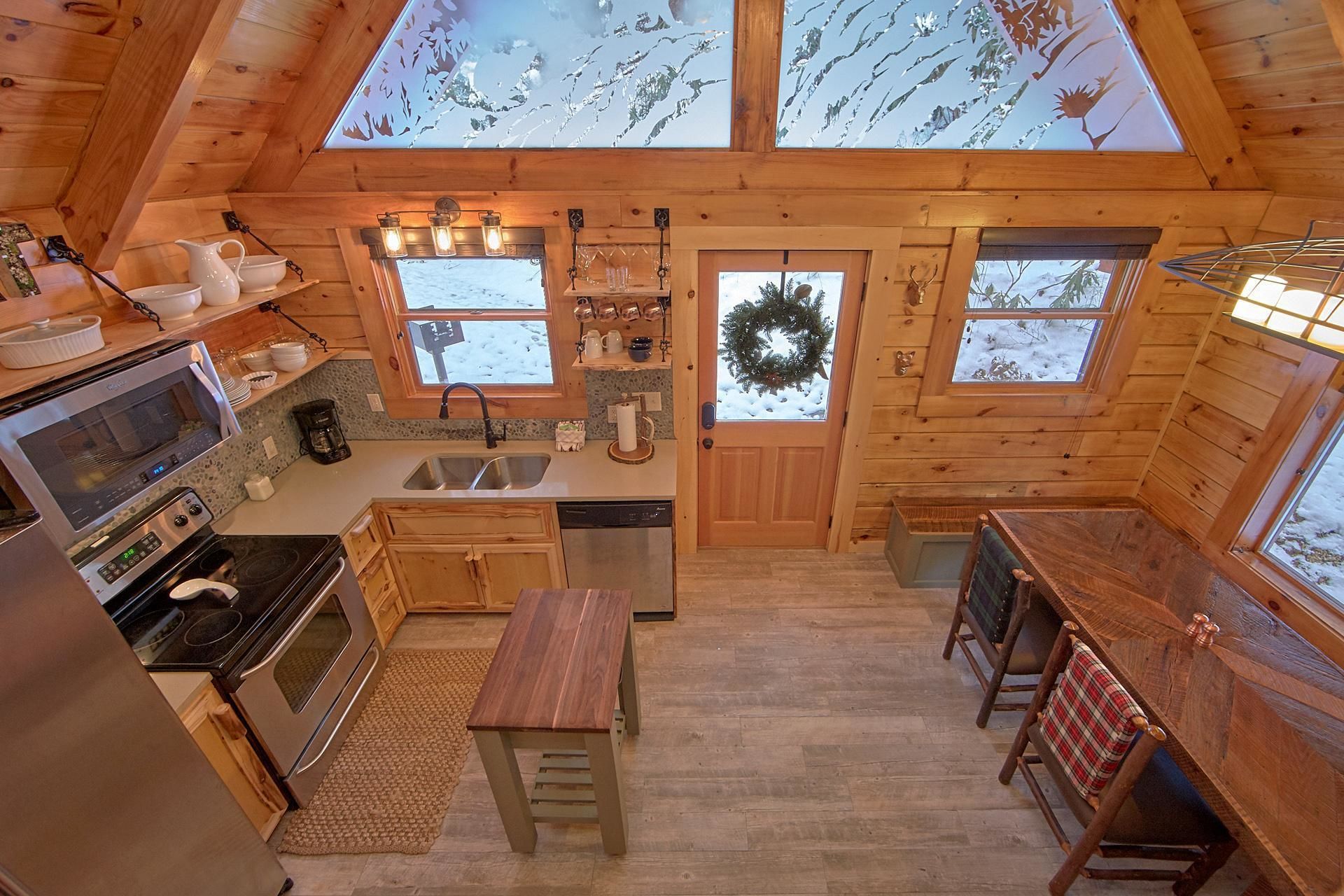 A cozy cabin kitchen with wooden walls, a central island, a microwave, stove, sink, and a dining area with benches.