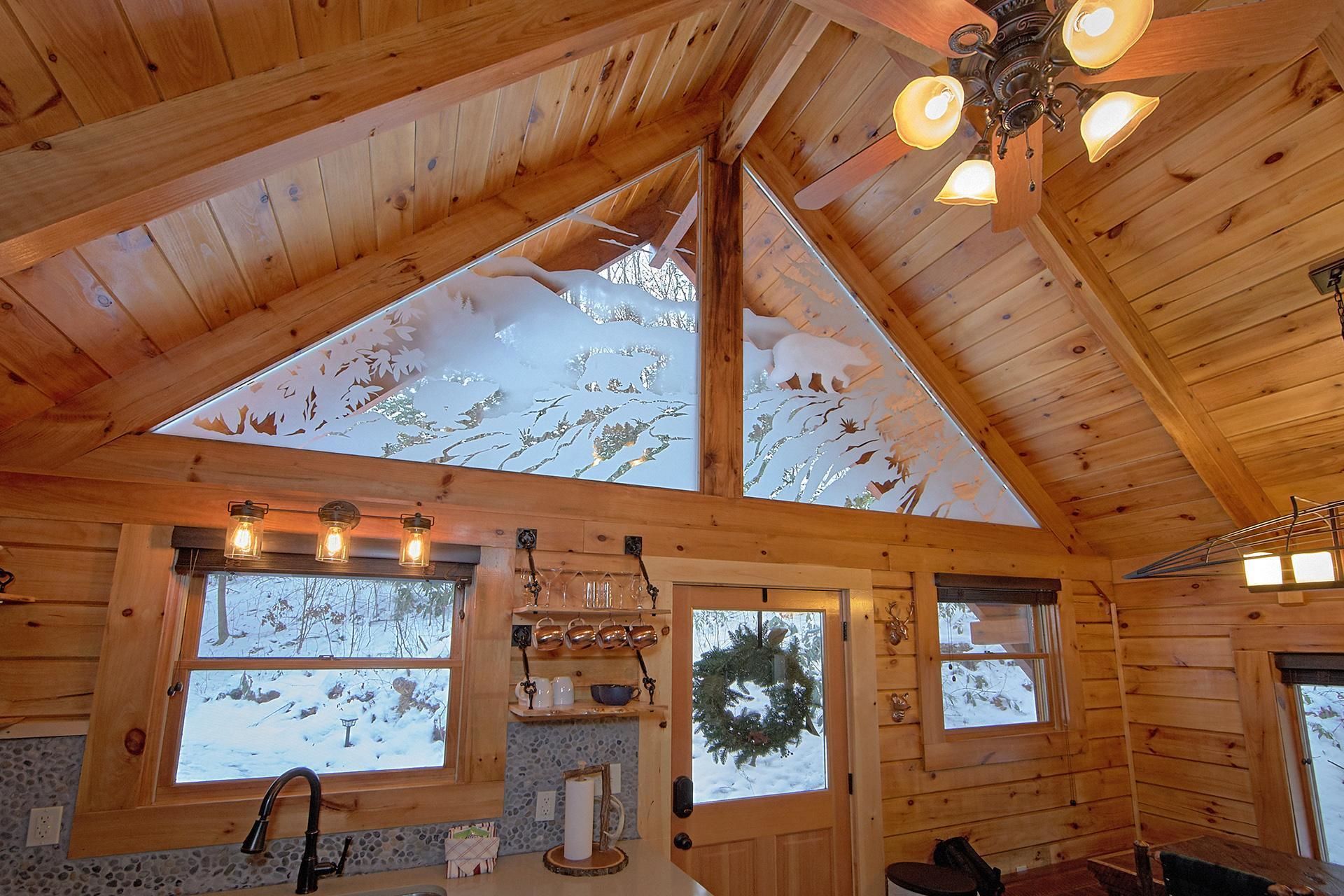 A log cabin interior with a sloped ceiling, wooden walls, and large windows.