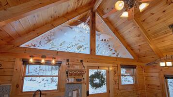 A log cabin interior with a sloped ceiling, wooden walls, and large windows.