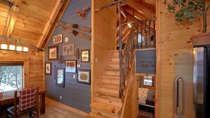 A wooden cabin interior with a staircase, framed pictures, and a refrigerator. - Foolin Around Apartment 1 (Sevierville)