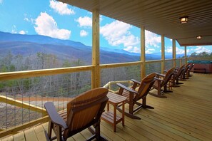 A covered deck with wooden chairs and a view of mountains. - Grand View Apartment 4 (Gatlinburg)