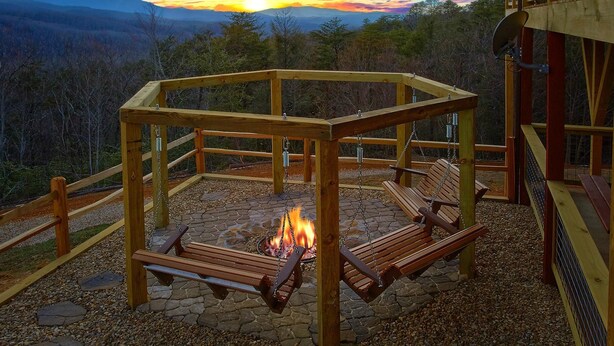 A wooden gazebo with benches and a fire pit, overlooking a mountainous landscape.