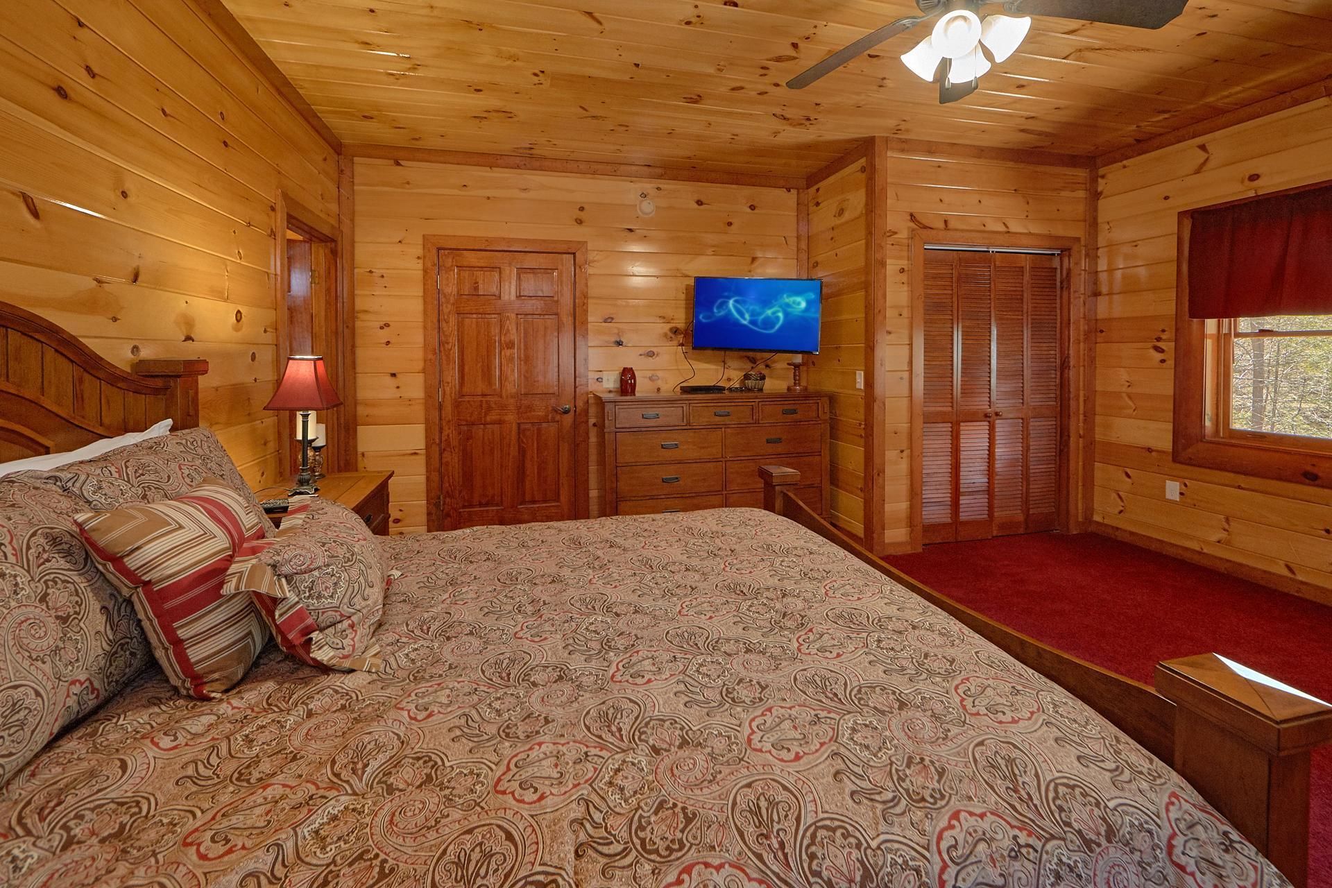 Ein Schlafzimmer einer Holzhütte mit Bett, Schminktisch, Fernseher und Fenster.