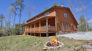 A two-story log cabin with a covered porch and a fire pit in front. - Sweet Tranquility Pool Lodge Apartment 4 (Cosby)