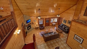 A wooden cabin interior with a fireplace, a TV, a sofa, and a staircase. - Sweet Tranquility Pool Lodge Apartment 4 (Cosby)