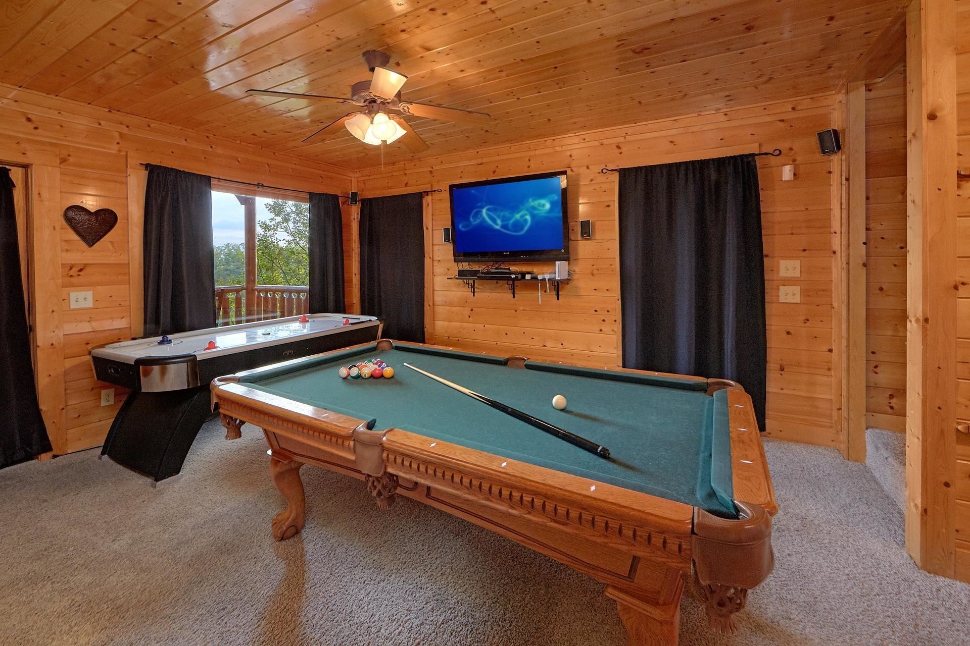 A wooden room with a pool table, a television mounted on the wall, and a ceiling fan.