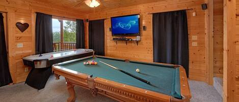 A wooden room with a pool table, a television mounted on the wall, and a ceiling fan.