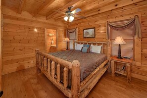A wooden cabin bedroom with a bed, two bedside lamps, a ceiling fan, and a window with blinds. - Legacy Vista Apartment 2 (Sevierville)