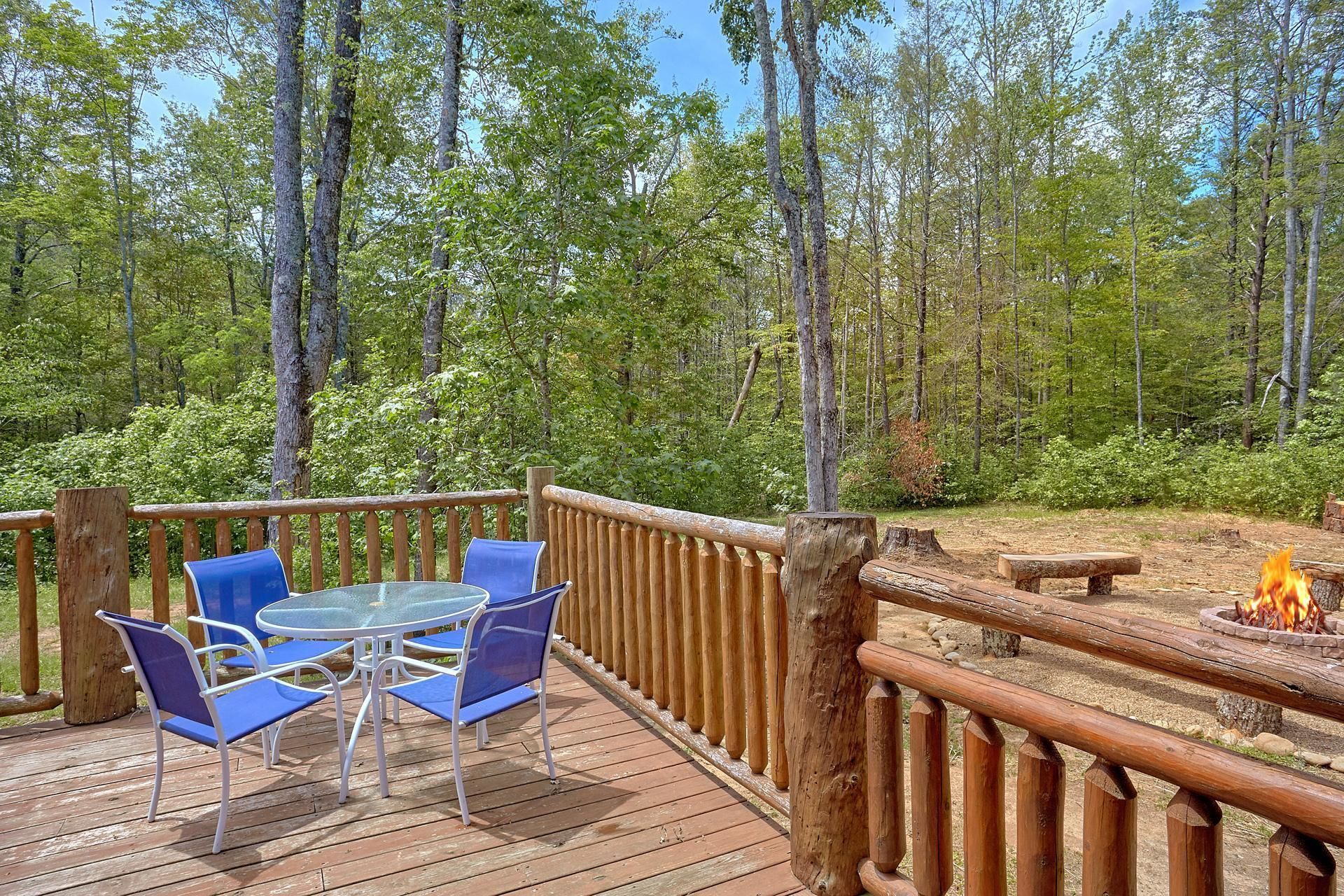 A wooden deck with a glass table and blue chairs, surrounded by a wooden fence and a fire pit.