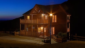 A two-story log cabin with a balcony and a porch, surrounded by a wooden fence.