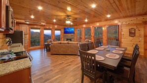 A wooden cabin interior with a kitchen, dining area, and a fireplace.