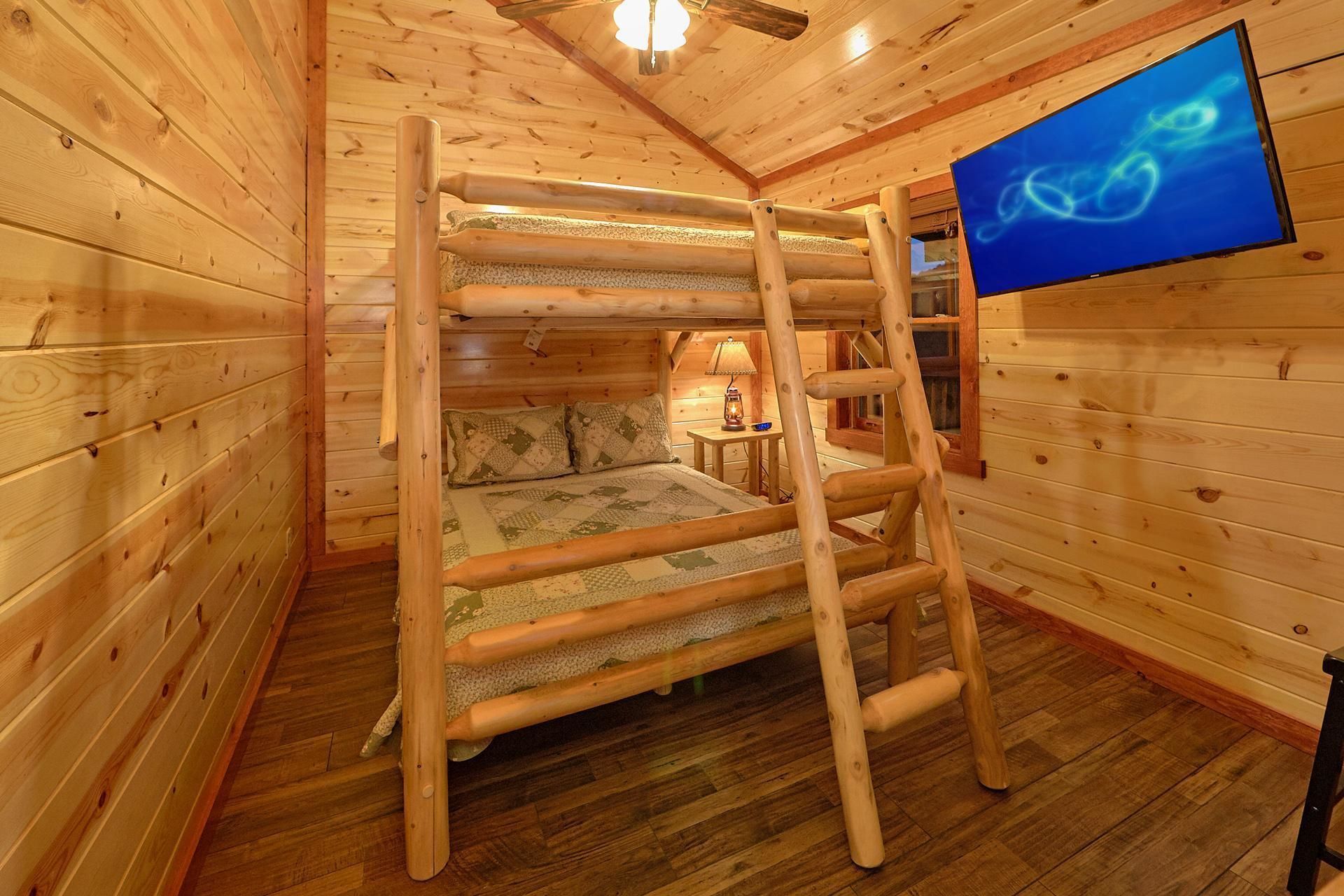 Una habitación tipo cabaña de madera con una litera, un televisor y una mesita de noche con lámpara.