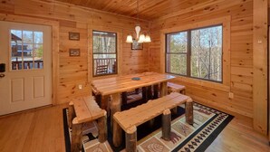 Ein Holzblock-Interieur mit einem Esstisch, Bänken und großen Fenstern, die einen Blick ins Freie bieten.