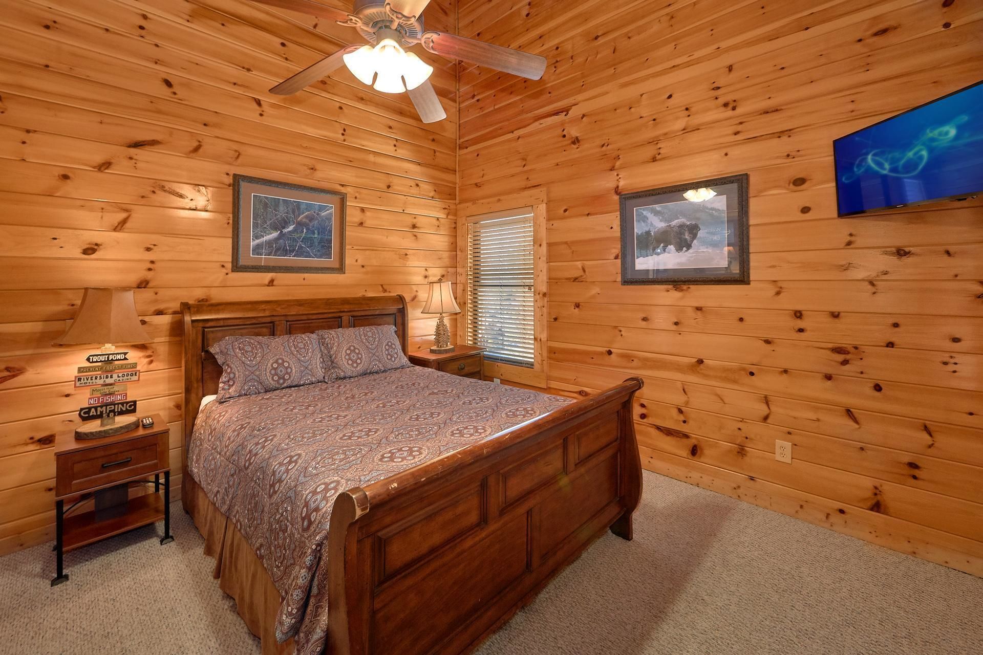 A wooden cabin bedroom with a bed, nightstand, lamp, and ceiling fan.