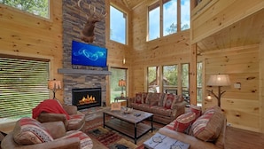 A cozy cabin interior with a stone fireplace, wooden walls, and a large TV mounted above it. - Big Sky Lodge Apartment 2 (Gatlinburg)