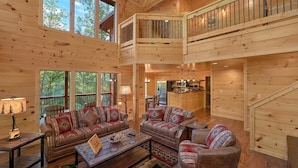 A spacious log cabin interior with a high ceiling, a dining area, a kitchen, and a balcony. - Big Sky Lodge Apartment 2 (Gatlinburg)