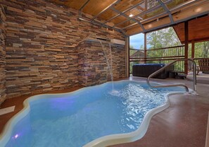 An indoor swimming pool with stone walls and a view of the outdoors.