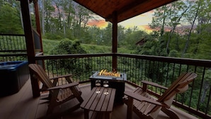A wooden deck with a fire pit and two chairs, surrounded by a metal railing and a view of a forested area. - Big Sky Lodge Apartment 2 (Gatlinburg)