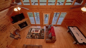Interior acogedor de una cabaña con chimenea, pisos de madera, un sofá, una mesa con juego de mesa y una mesa de billar.