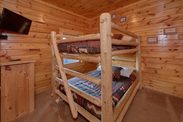 A bunk bed room with wooden walls and a television mounted on the wall.