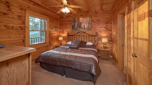 Dormitorio de una cabaña de madera con cama, dos lámparas de noche, ventilador de techo y ventana.