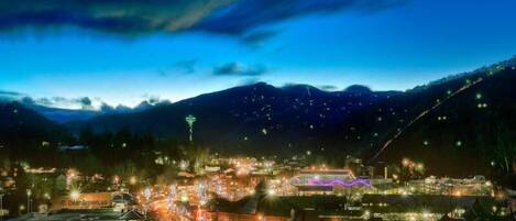 A town at night with illuminated buildings and a mountain in the background.