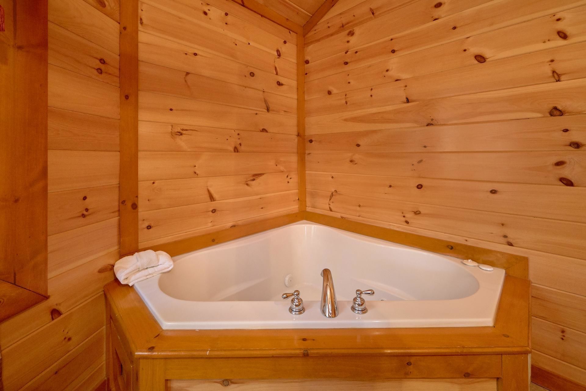 A wooden cabin with a corner bathtub, wooden walls, and a wooden floor.
