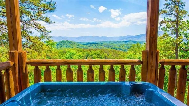 Jacuzzi en una terraza de madera con vistas a una cadena montañosa boscosa.