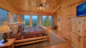 Un dormitorio de cabaña de troncos con una cama, un televisor y vistas a las montañas.
