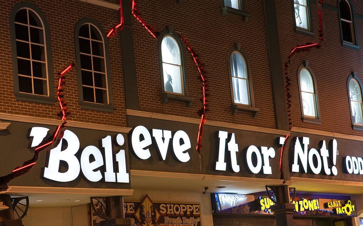 En bygnings facade med store, oplyste skilte, der viser teksten "Believe It or Not!" og "SHOPPE Fresh Daily".