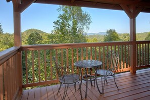 A wooden deck with two metal tables and chairs, overlooking a mountainous landscape. - Time Stands Still Apartment 3 (Sevierville)