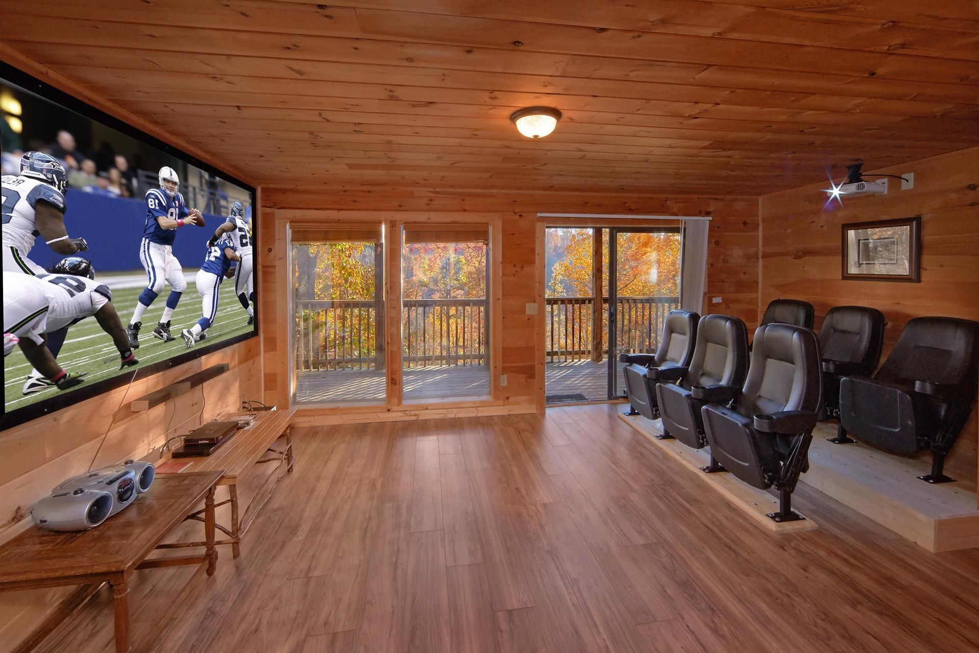 Interno di una baita in legno con un grande schermo televisivo che mostra una partita di calcio, una panca di legno e una fila di sedie.