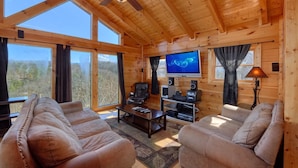 Un intérieur de chalet chaleureux avec deux canapés en cuir, un téléviseur et un ventilateur de plafond.