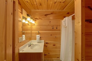 A wooden cabin bathroom with a sink, mirror, and towel hanging on hooks.
