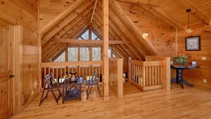 L’intérieur d’un chalet en bois comprend un coin repas, une cheminée et une grande fenêtre.