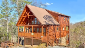 Une cabane en rondins à deux étages, dotée d’une terrasse en bois et d’un porche couvert.