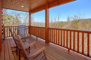 A wooden deck with a barbecue grill and two wooden chairs.