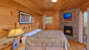 Une chambre dans un chalet en bois, avec un lit, une télévision, une cheminée et une fenêtre.