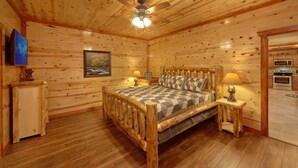 A wooden cabin room with a bed, a ceiling fan, a painting, a television, and a kitchenette. - Summit Pool Lodge Apartment 6 (Gatlinburg)
