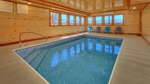 An indoor swimming pool with clear blue water, wooden walls, and windows offering a view of the outdoors. - Summit Pool Lodge Apartment 6 (Gatlinburg)