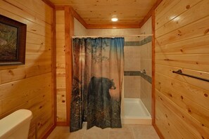 Une salle de bain aux murs lambrissés, équipée d’une douche, de toilettes et d’un tableau encadré.