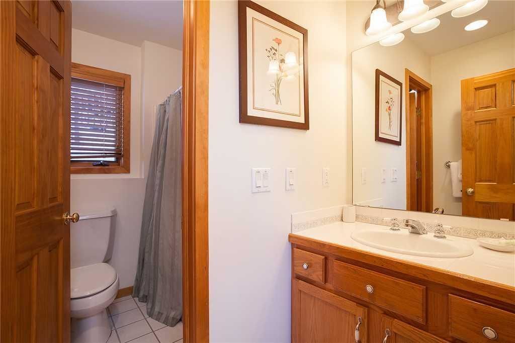 A bathroom with a toilet, shower, sink, and wooden cabinets.