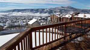 Un hôtel doté d’une terrasse en bois et de sièges extérieurs, offrant une vue sur une ville et des montagnes recouvertes de neige.