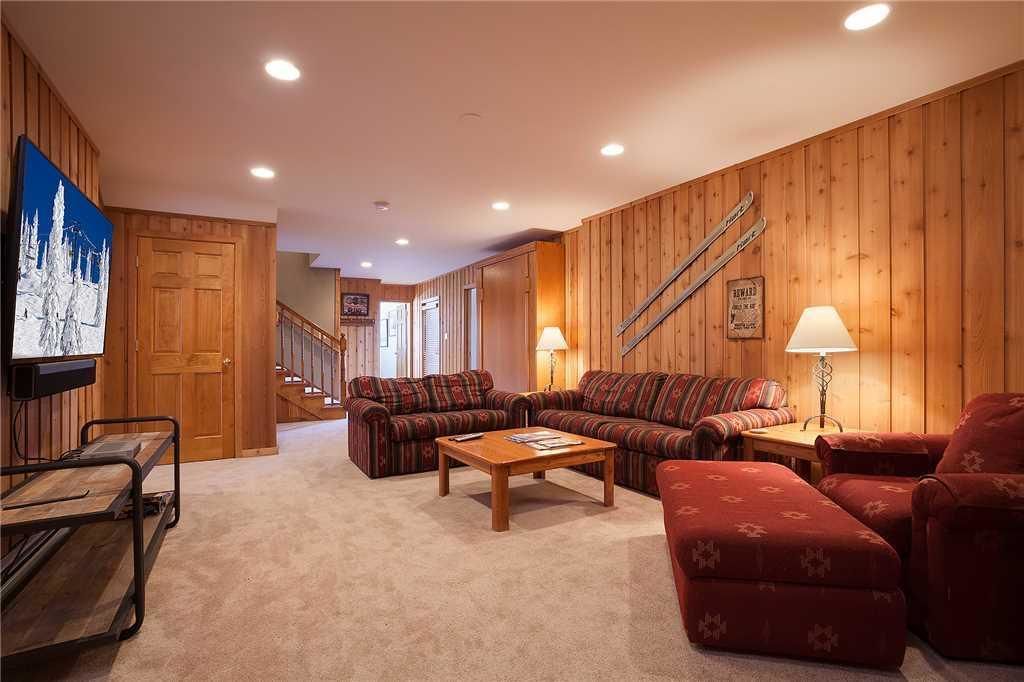 A cozy living room with wooden paneling, a sofa set, a coffee table, and a TV on the left wall.