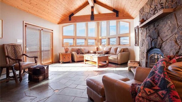 Un salon chaleureux avec une cheminée en pierre, un plafond en bois et de grandes fenêtres.
