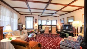 A traditional living room with a red floral carpet, wooden furniture, a piano, and a fireplace. - Luther Ogden Inn (Cape May)