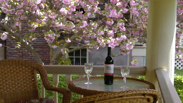 A wicker chair and table with a bottle of wine and two glasses on a balcony. - Luther Ogden Inn (Cape May)