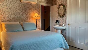 A bedroom with a bed, a bedside lamp, a white door, a wall-mounted mirror, and a wall-mounted air conditioner.