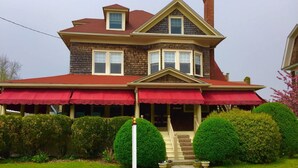 A two-story house with a red roof, a front porch with red awnings, and a chimney. - Luther Ogden Inn (Cape May)