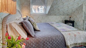 A bedroom with a bed, a window, a nightstand, and a vase of tulips. - Luther Ogden Inn (Cape May)